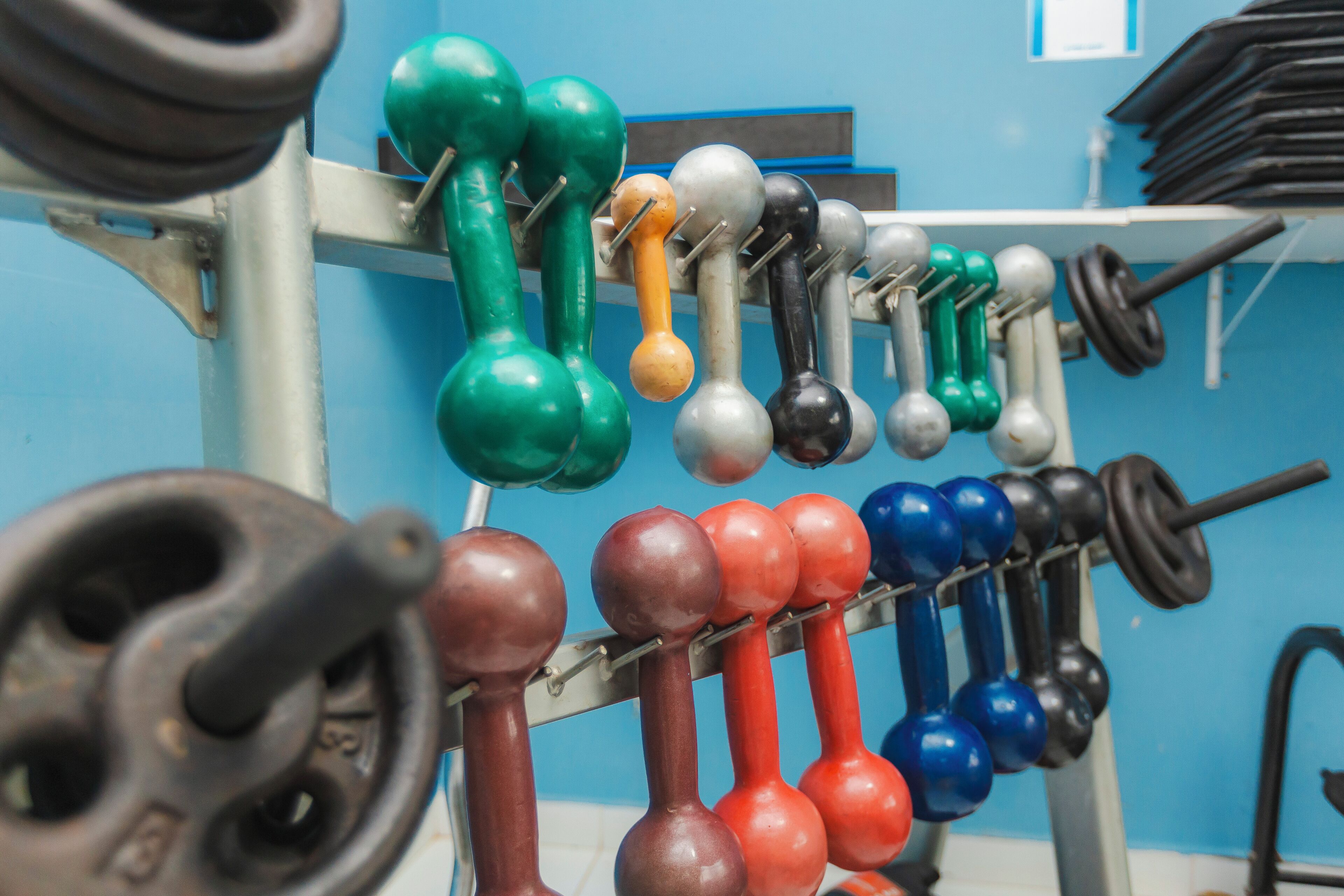 A rack of variously colored dumbbells in a gym setting.