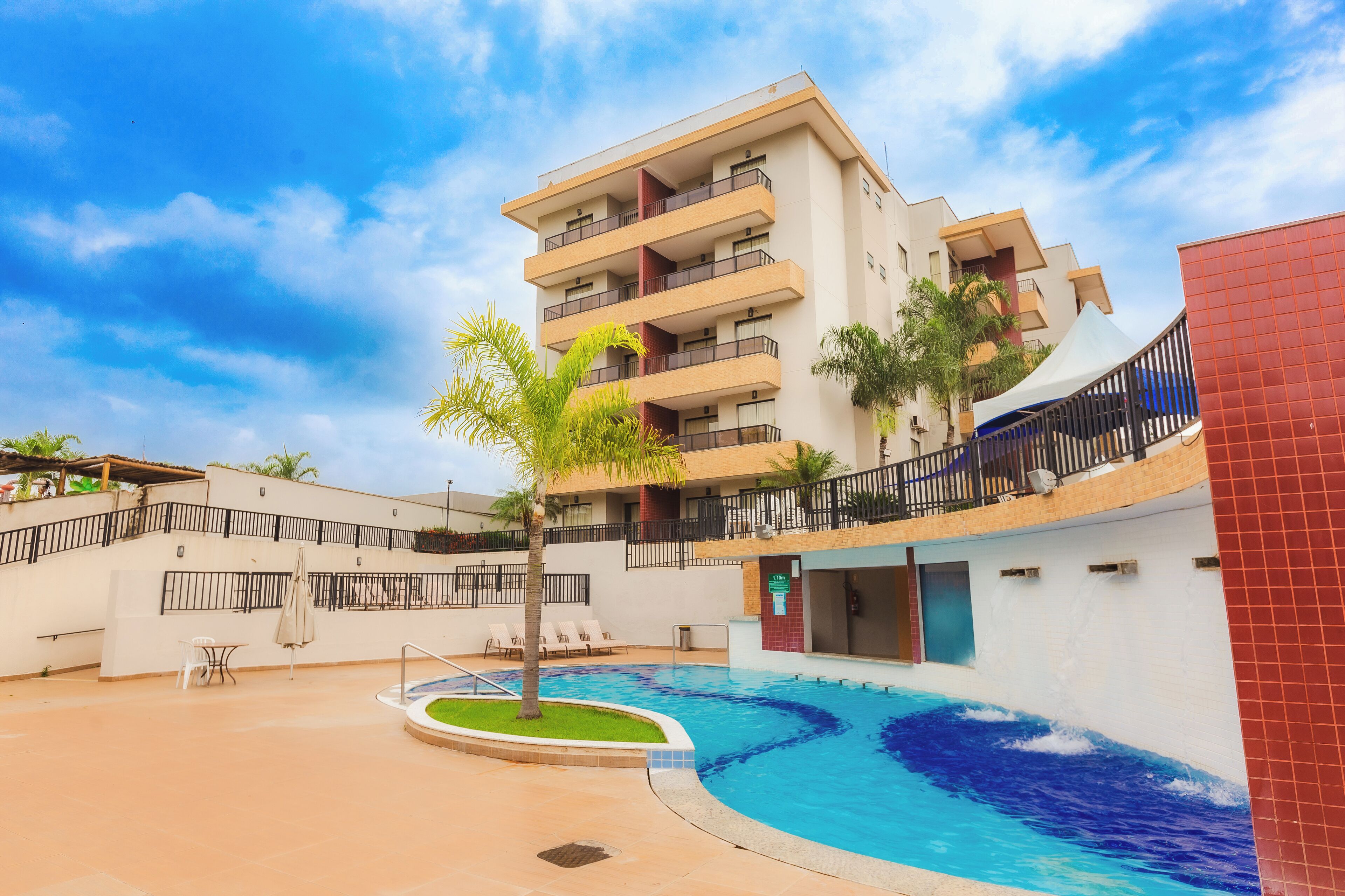 A hotel with a swimming pool, outdoor seating, and a multi-story building.