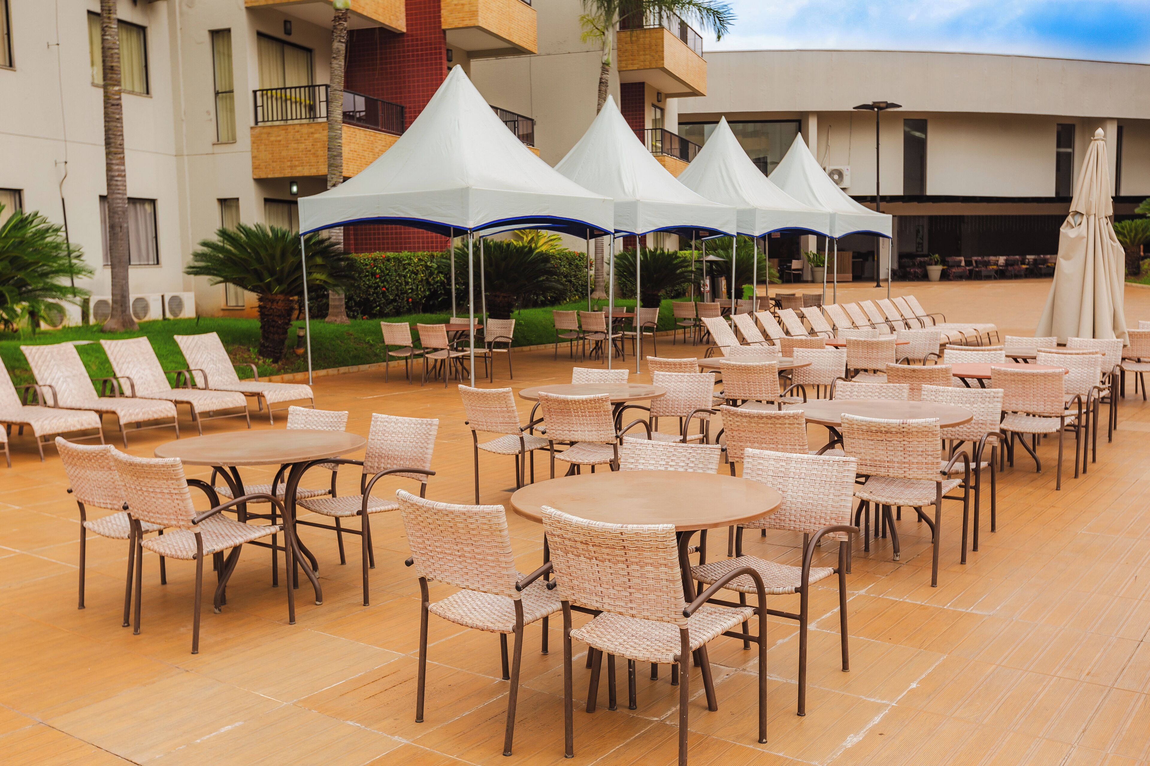 An outdoor seating area with round tables and wicker chairs, surrounded by white canopies.