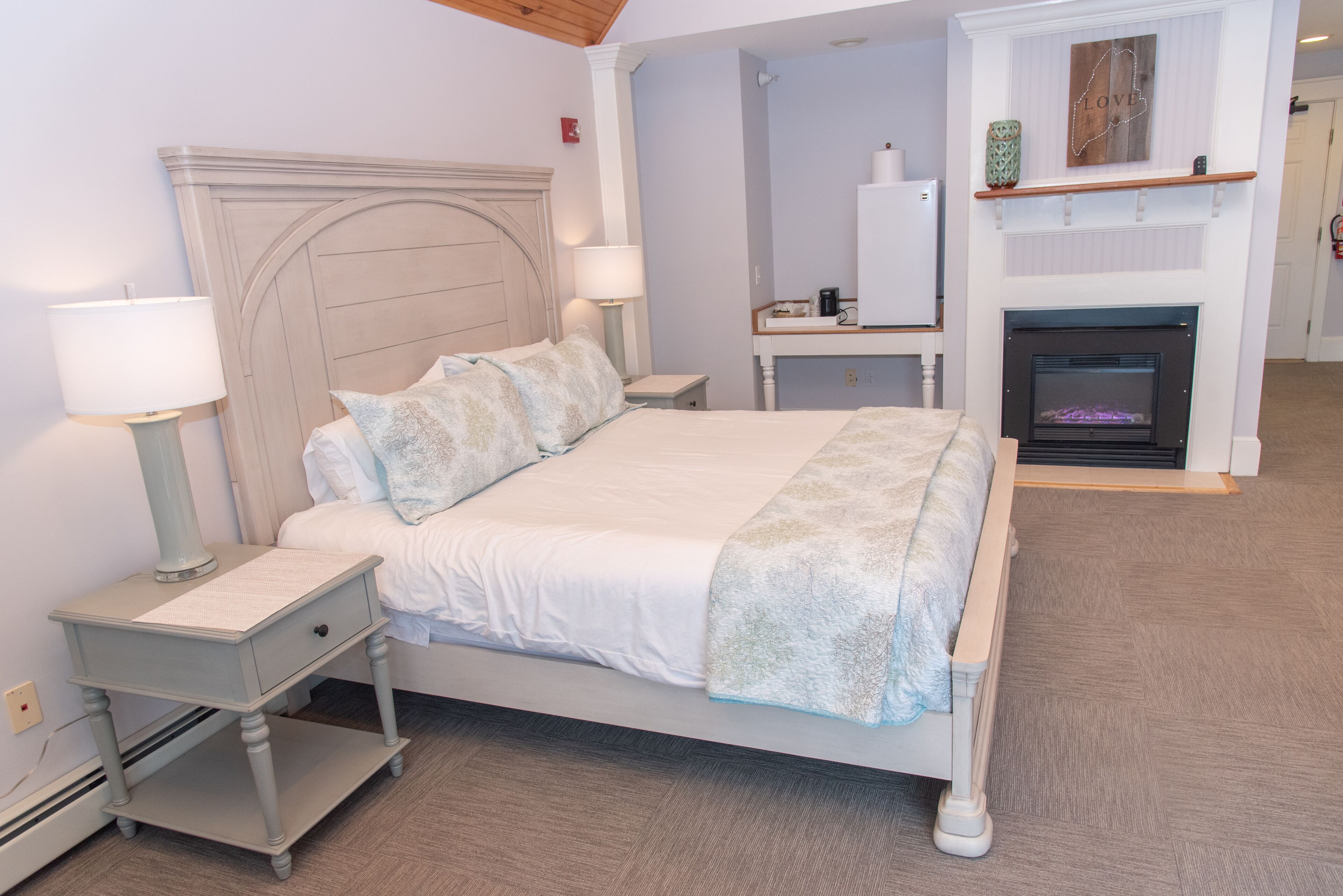 A bedroom with a bed, nightstands, a dresser, a fireplace, and a mirror.