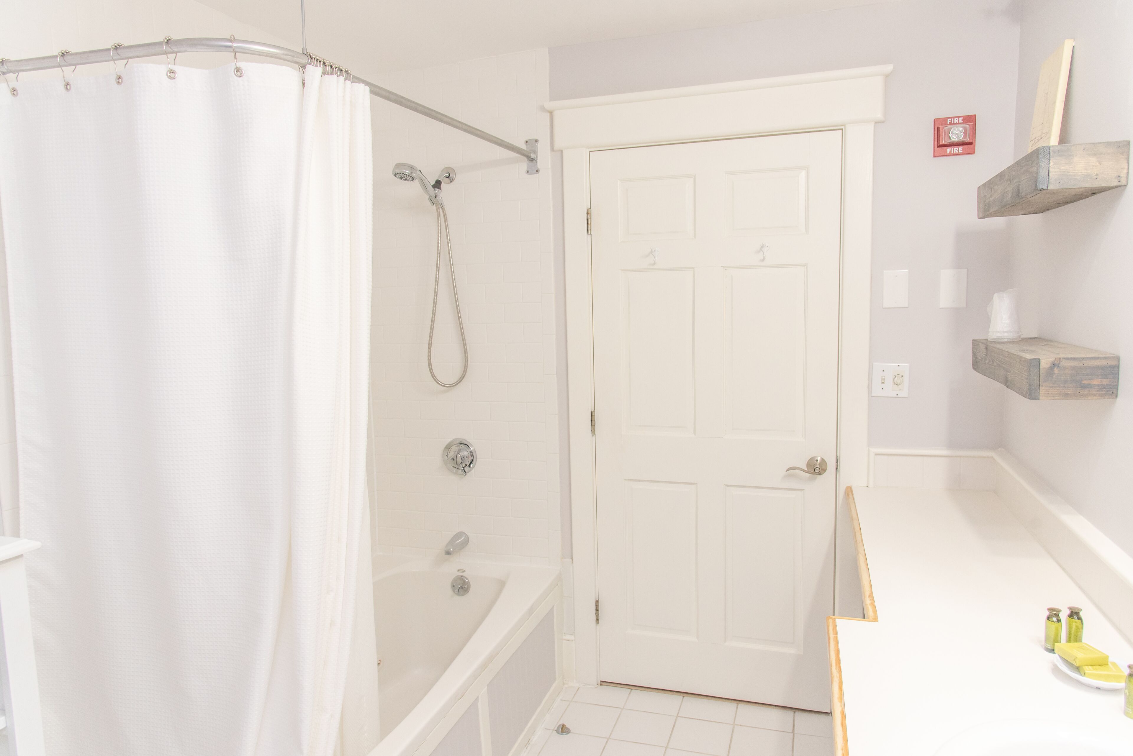 A bathroom with a shower, a bathtub, a white door, and a shelf with toiletries.