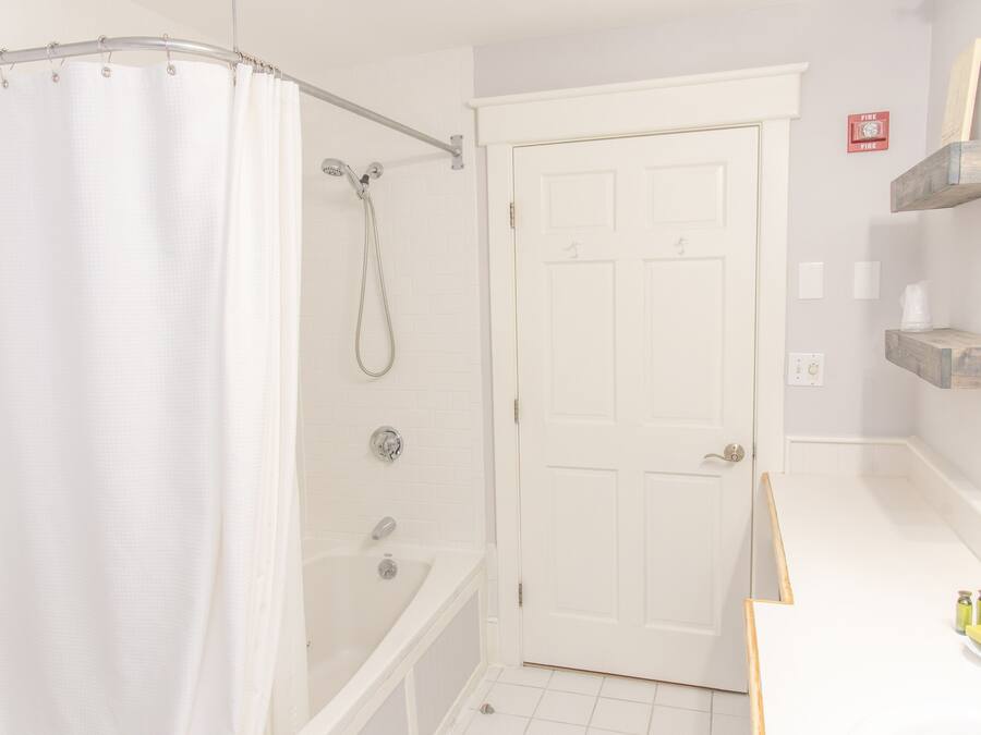 A bathroom with a shower, a bathtub, a white door, and a shelf with toiletries.