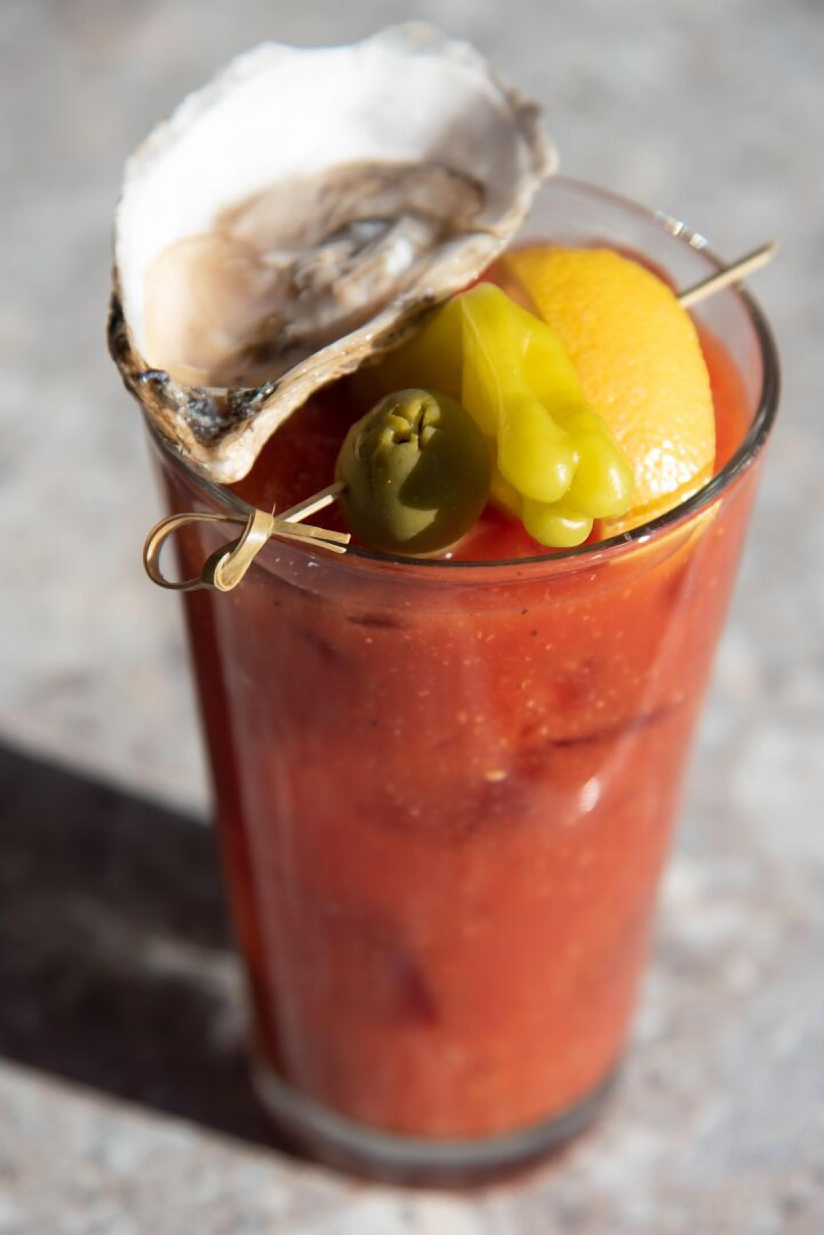A glass of Bloody Mary with an oyster and olives.