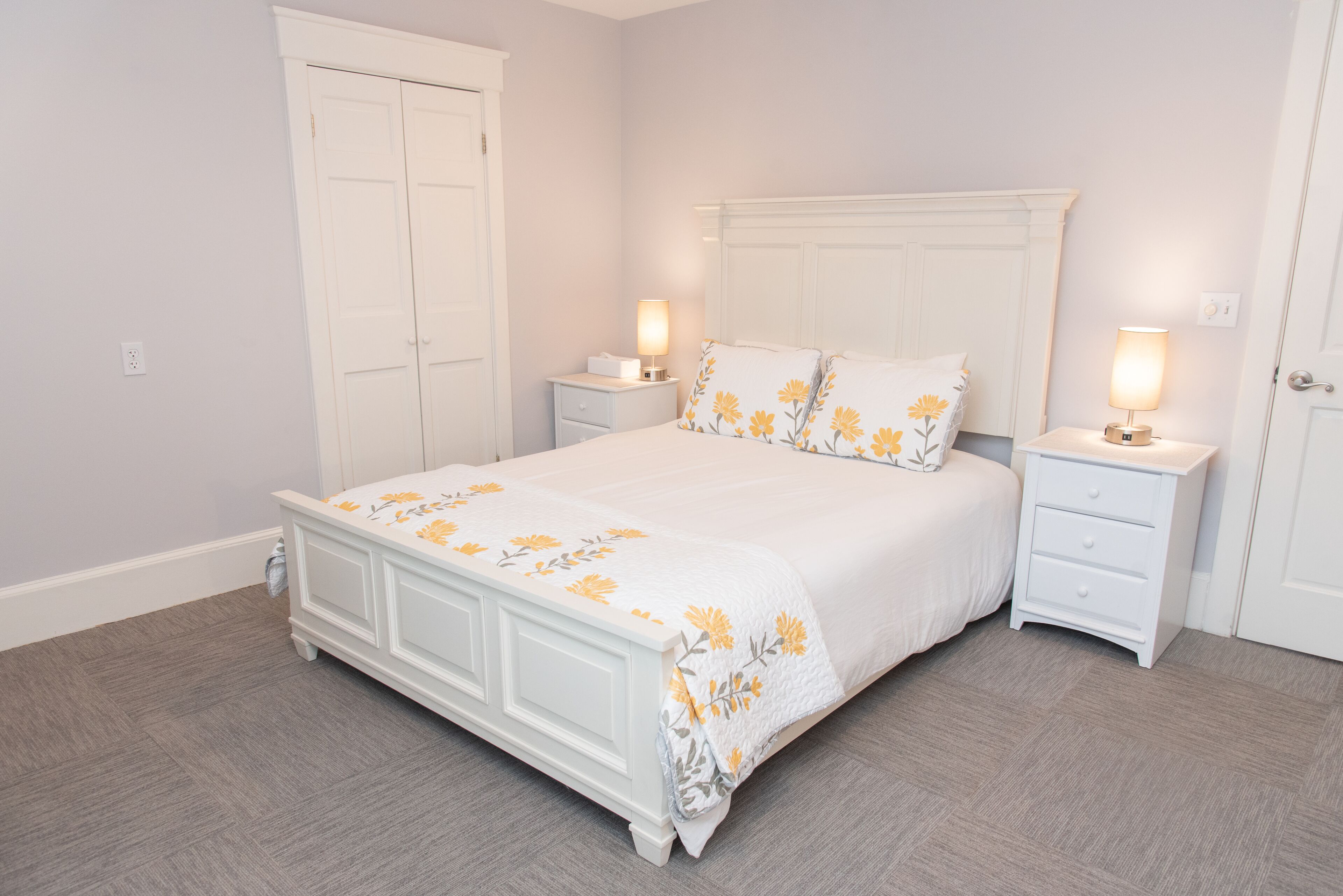 Un dormitorio con una cama blanca, dos mesitas de noche y un armario blanco.