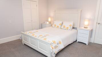 Un dormitorio con una cama blanca, dos mesitas de noche y un armario blanco.