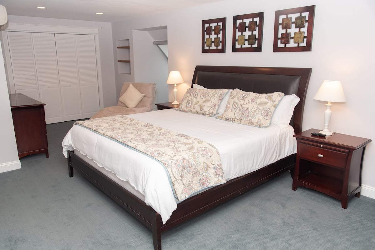 A bedroom with a large bed, two bedside tables, a wardrobe, and a chair.