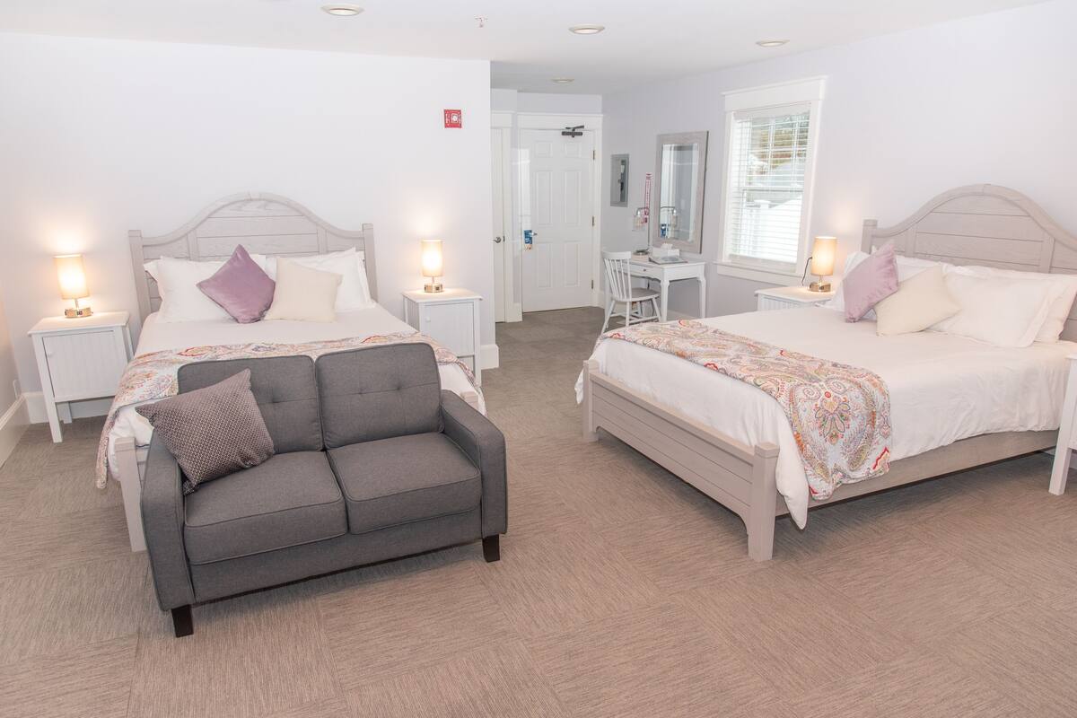 A hotel room with two beds, a desk, a chair, and a sofa.