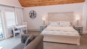 A bedroom with a large bed, two bedside tables with lamps, a round table with chairs, and a grey sofa. - Inn On Peaks Island (Peaks Island)