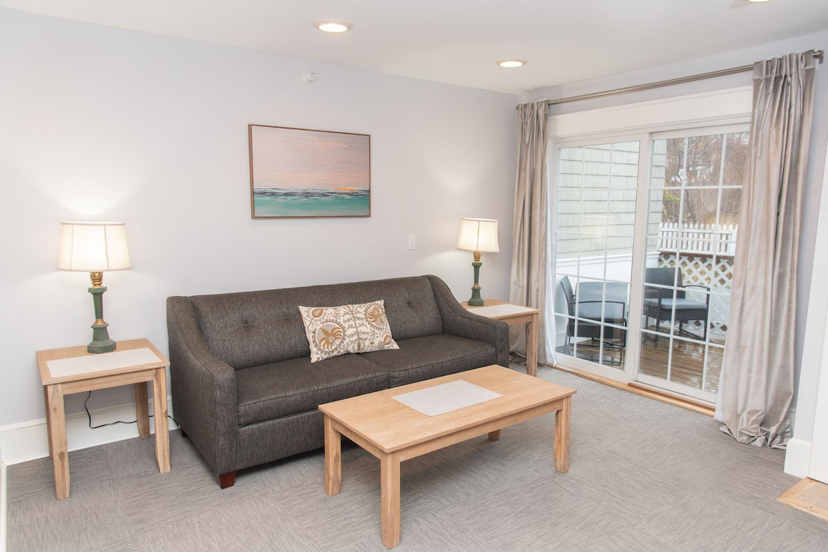 A living room with a sofa, two side tables with lamps, a coffee table, and a large window with curtains.