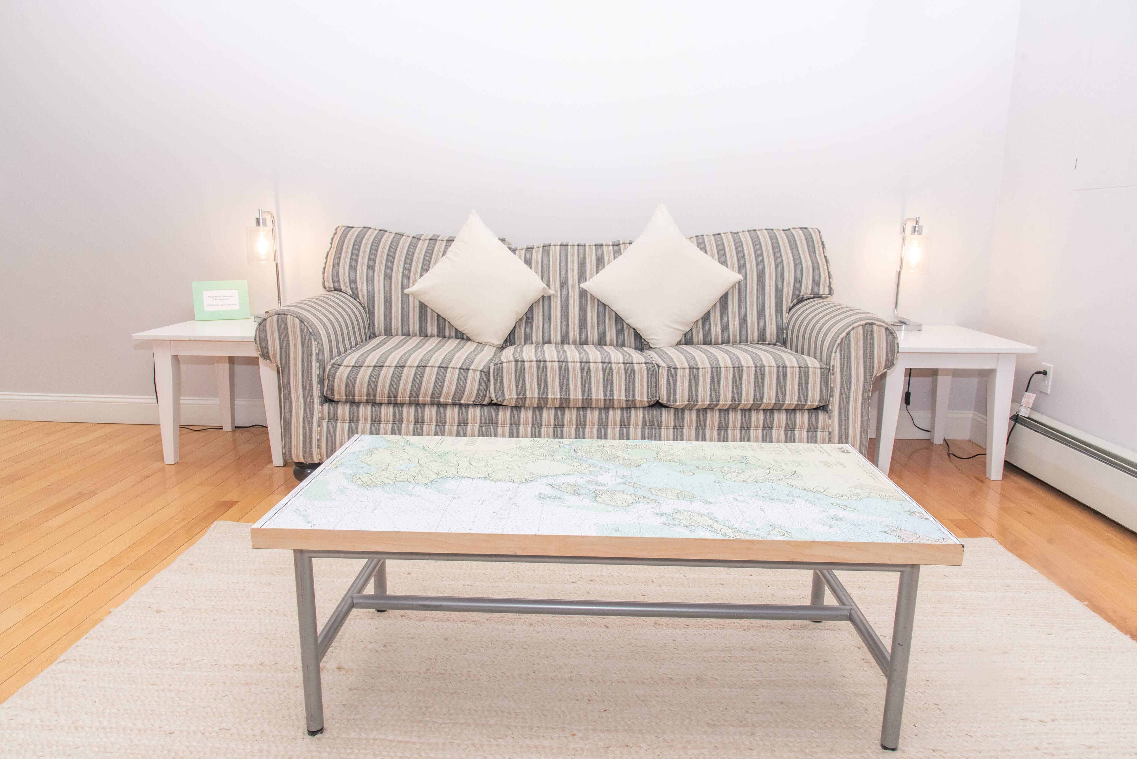 A living room with a striped sofa, two white pillows, a wooden coffee table with a map, and two bedside lamps on white nightstands.