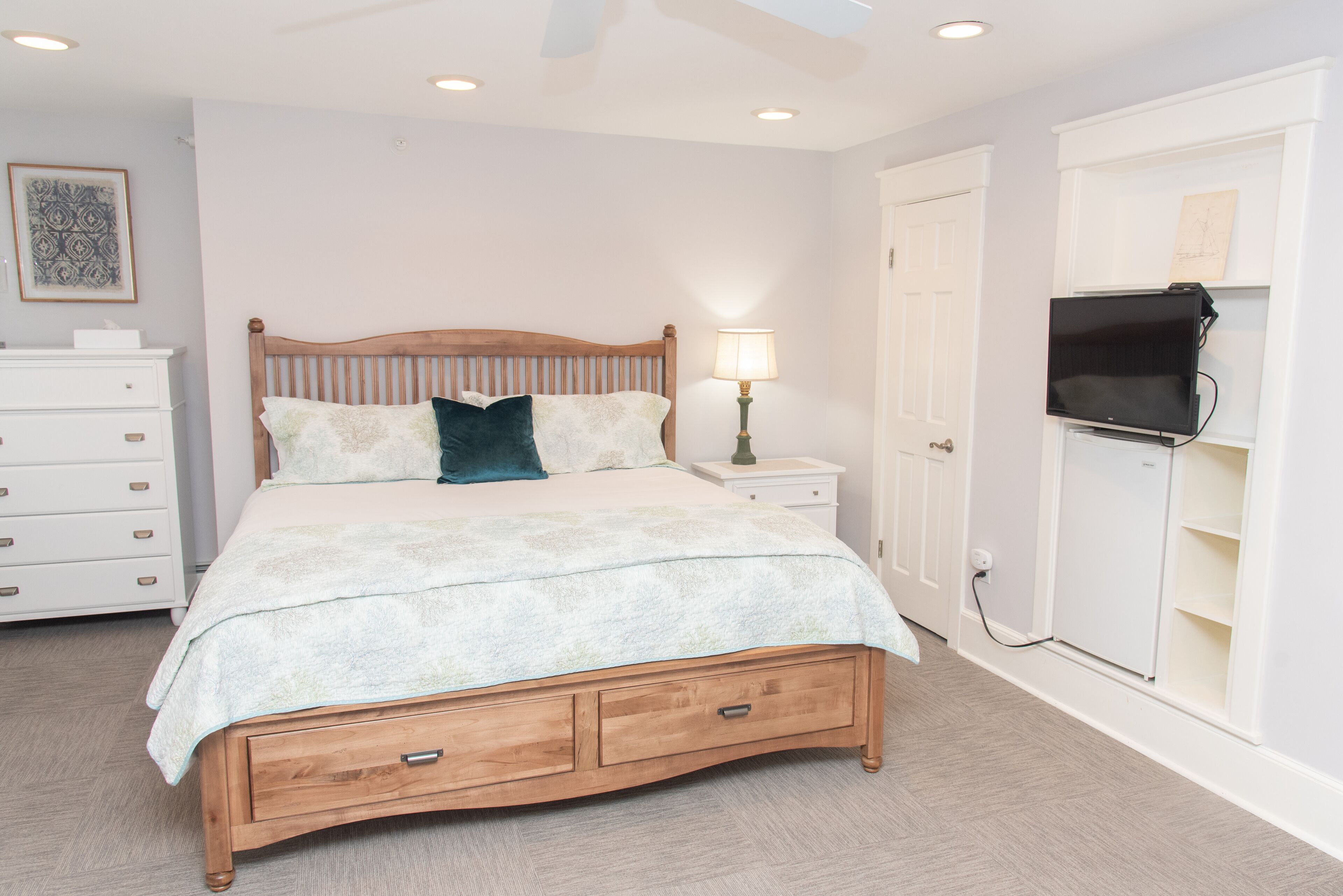 A bedroom with a wooden bed, bedside lamp, TV, and a dresser.