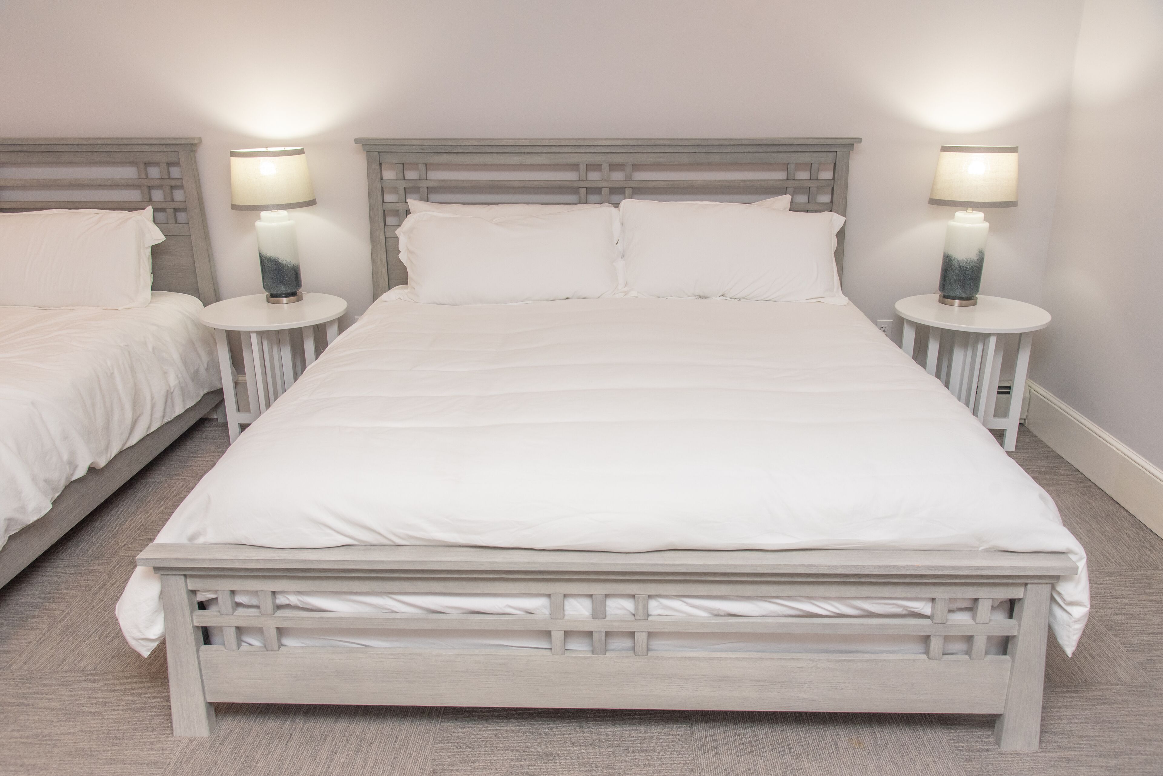 A double bed with a wooden frame, two bedside tables with lamps, and white bedding.