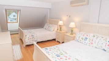 A bedroom with two single beds, wooden flooring, a window with a view, and a wall-mounted air conditioner.