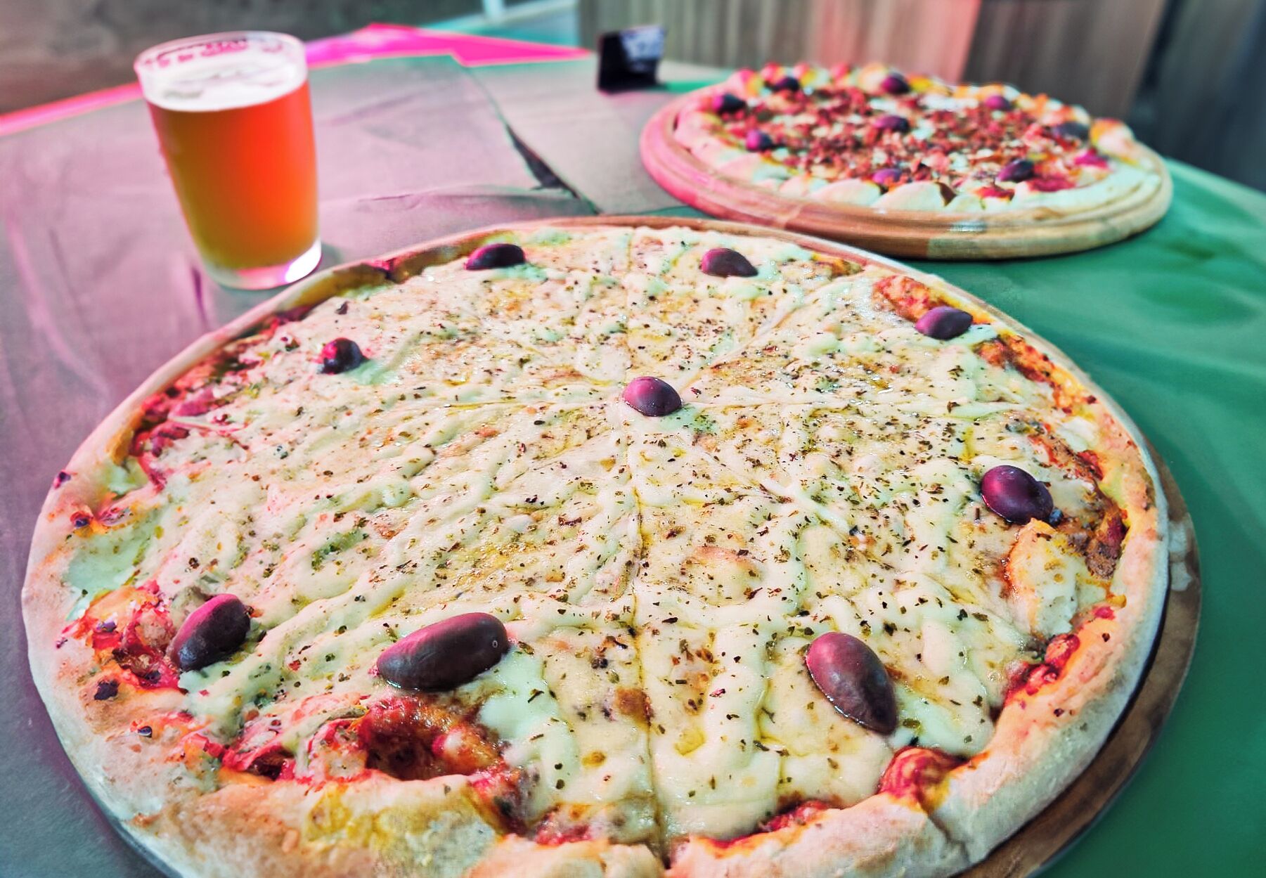 Duas pizzas sobre uma mesa com um copo de cerveja.