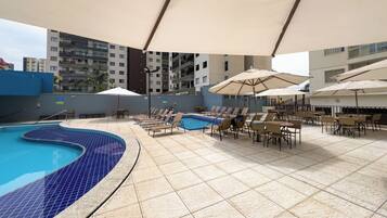 A rooftop pool area with lounge chairs and umbrellas, surrounded by buildings.