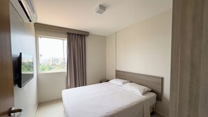 A hotel room with a bed, a TV mounted on the wall, a window with curtains, and an air conditioning unit. - Hotel Atrium Thermas - Oficial (Caldas Novas)