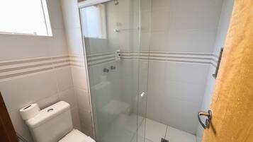 A bathroom with a glass-enclosed shower, a toilet, and a window.
