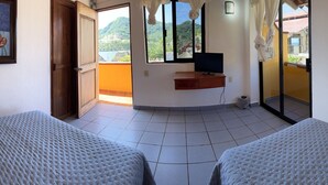 Un couloir d’hôtel avec deux lits, un téléviseur et une vue sur un paysage montagneux par la fenêtre.