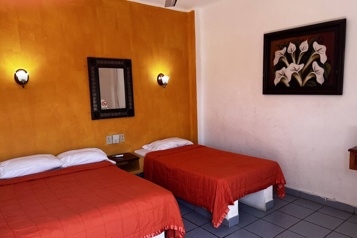 Habitación de hotel con dos camas, un espejo, luces fijadas a la pared, un cuadro y suelo de baldosas.