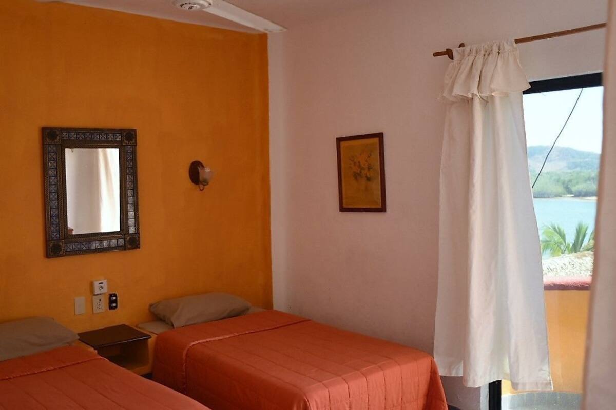 Una habitación con dos camas, un espejo, un cuadro en la pared y una ventana con cortina.