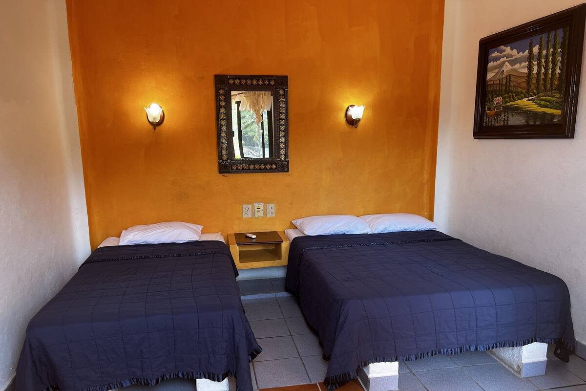 Una habitación con dos camas, una mesita de noche, un espejo en la pared y un cuadro.