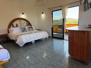 Un dormitorio con cama, mesita de noche, escritorio de madera y vistas al exterior.