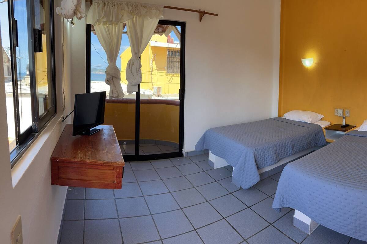 Una habitación con dos camas, un escritorio de madera, una silla y una ventana con cortinas.