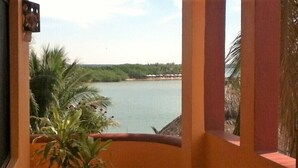 Une vue depuis un balcon doté d’une balustrade, donnant sur une étendue d’eau calme et sur une côte lointaine bordée de végétation.