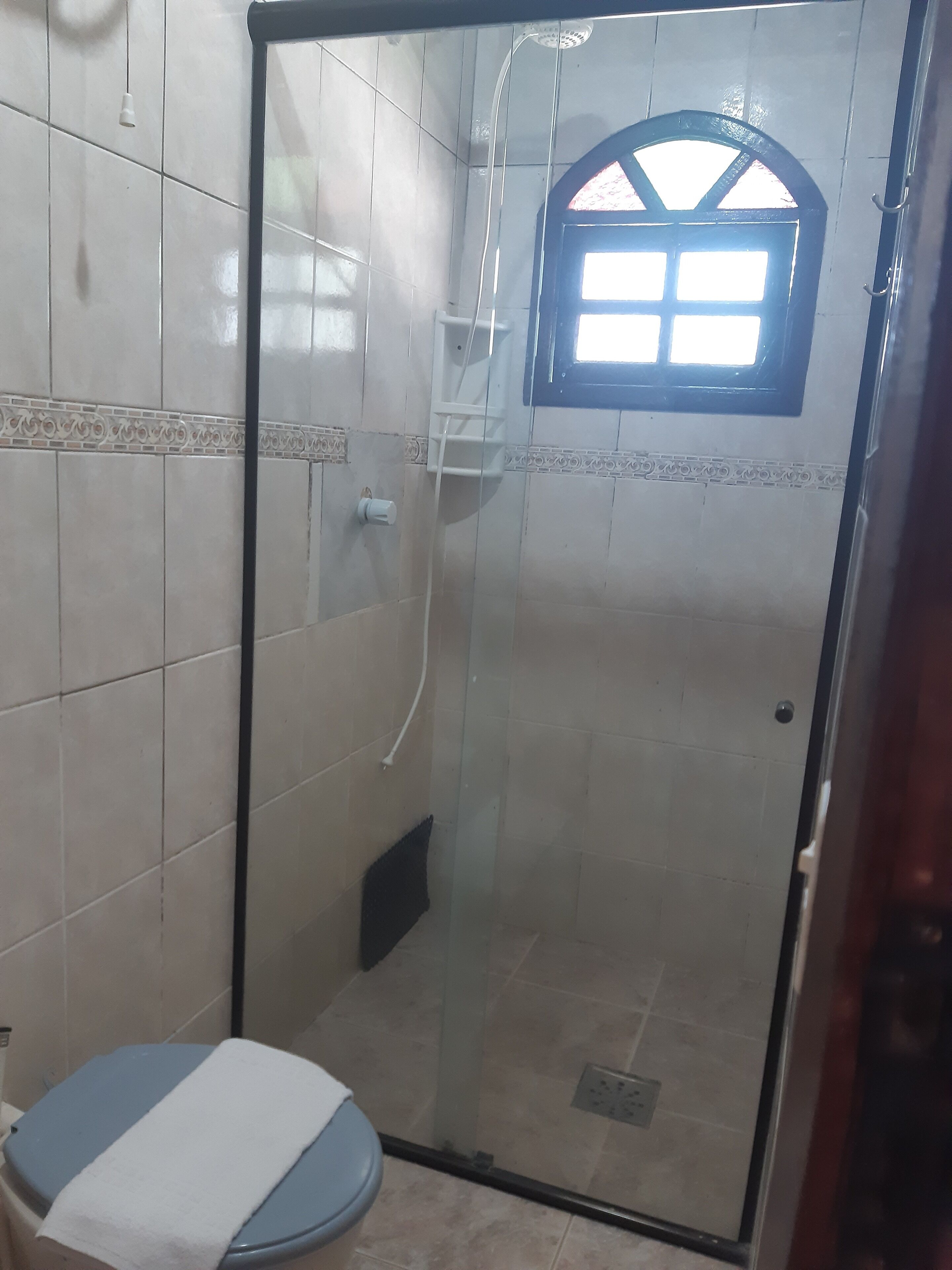 A small, enclosed shower area with a glass door, a window, and a toilet with a towel on it.