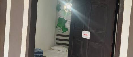Una habitación con una cama, una lámpara fijada a la pared y una puerta con un letrero que dice 'Jasmin'.