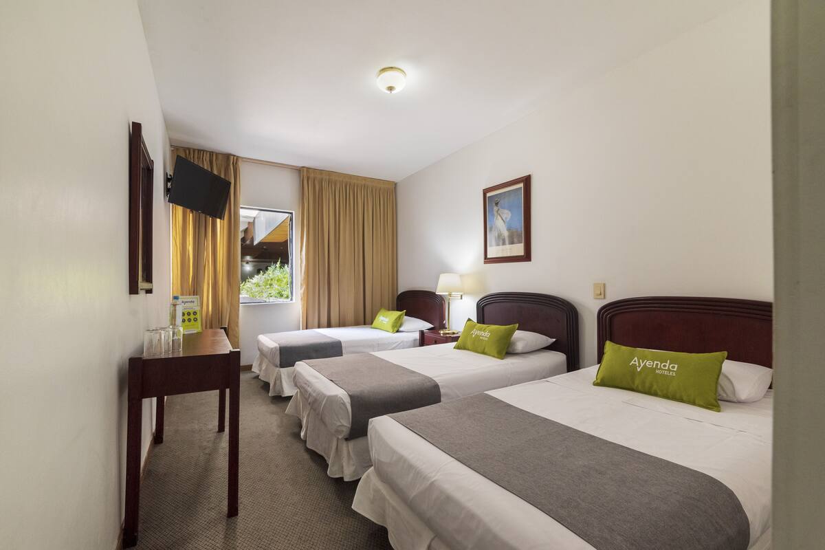 A hotel room with two beds, a desk, a TV, and a window with curtains.