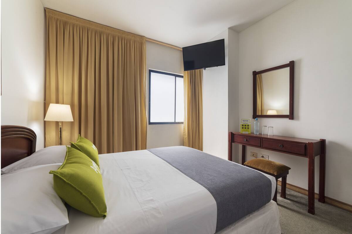 A hotel room with a bed, a desk, a chair, a TV, and a window.