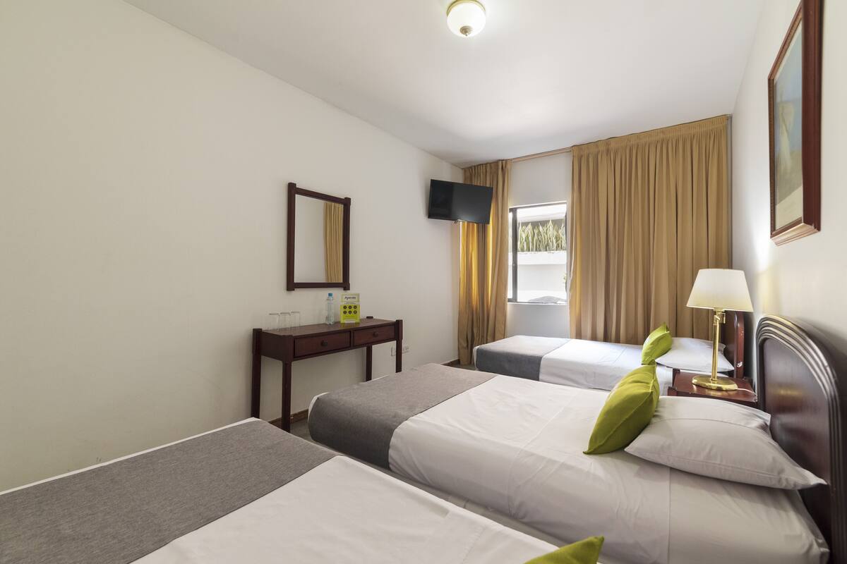 A hotel room with two single beds, a desk with a chair, a television mounted on the wall, and a window with curtains.