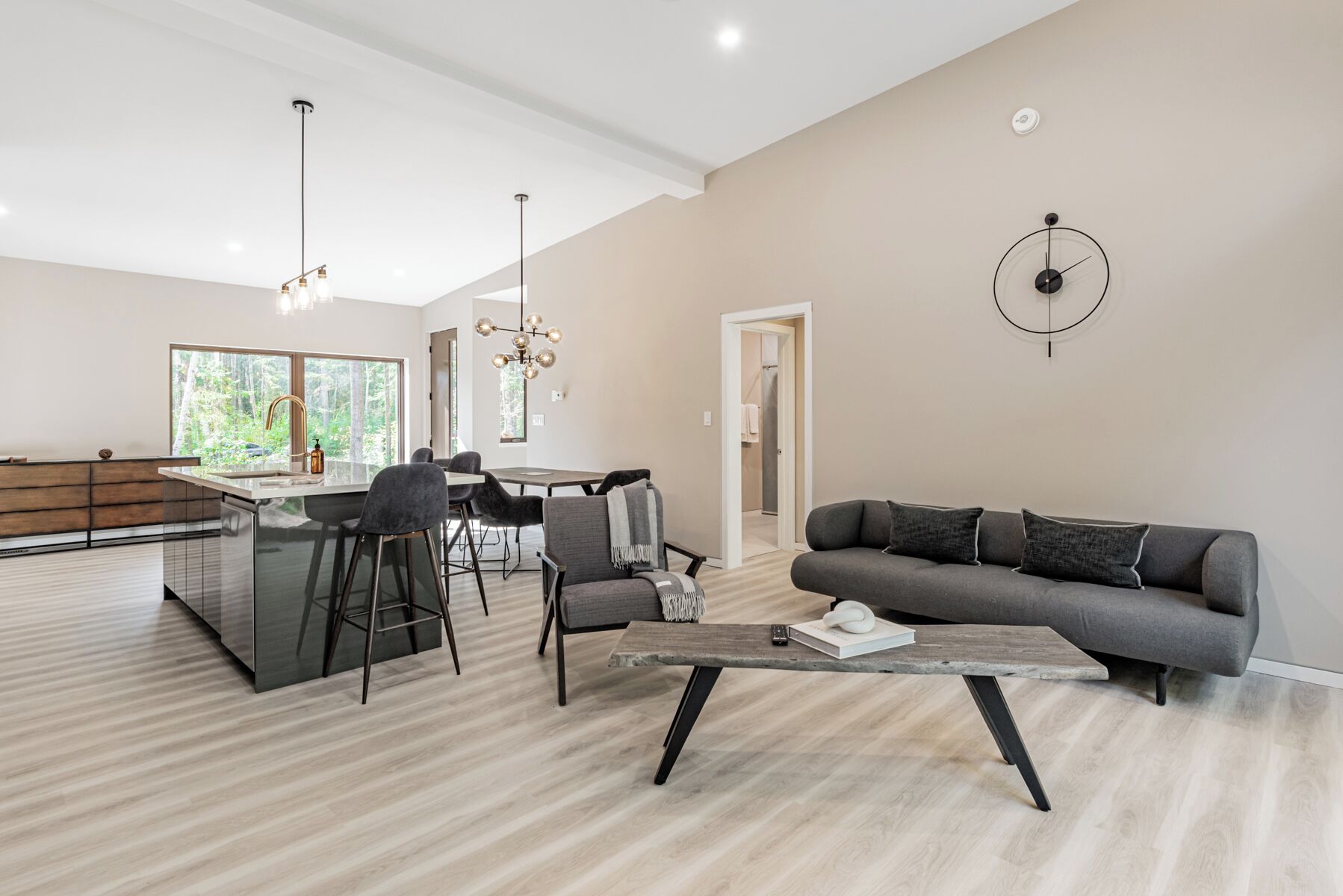 A modern living room with a grey sofa, a coffee table, and a dining area with a large window.