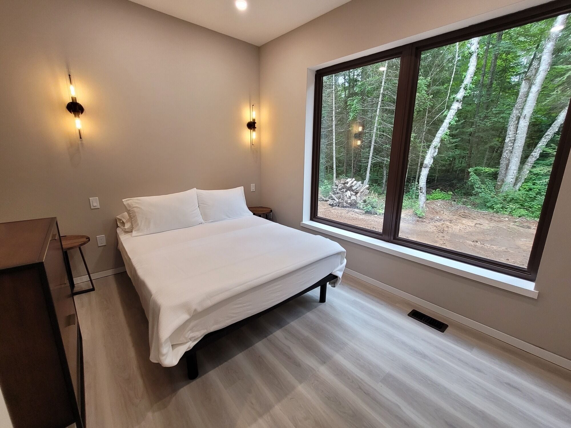 Un dormitorio con un ventanal grande, una cama y dos luces fijadas a la pared.
