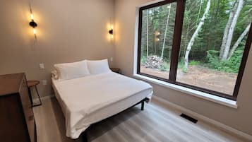 Un dormitorio con un ventanal grande, una cama y dos luces fijadas a la pared.