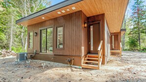 Una cabaña moderna de madera con grandes puertas corredizas de vidrio, un porche cubierto y suelo de tierra.