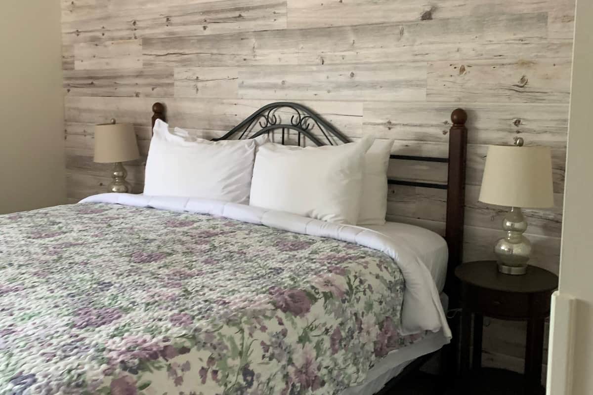 A bedroom with a wooden headboard, a floral bedspread, two bedside lamps, and a nightstand.