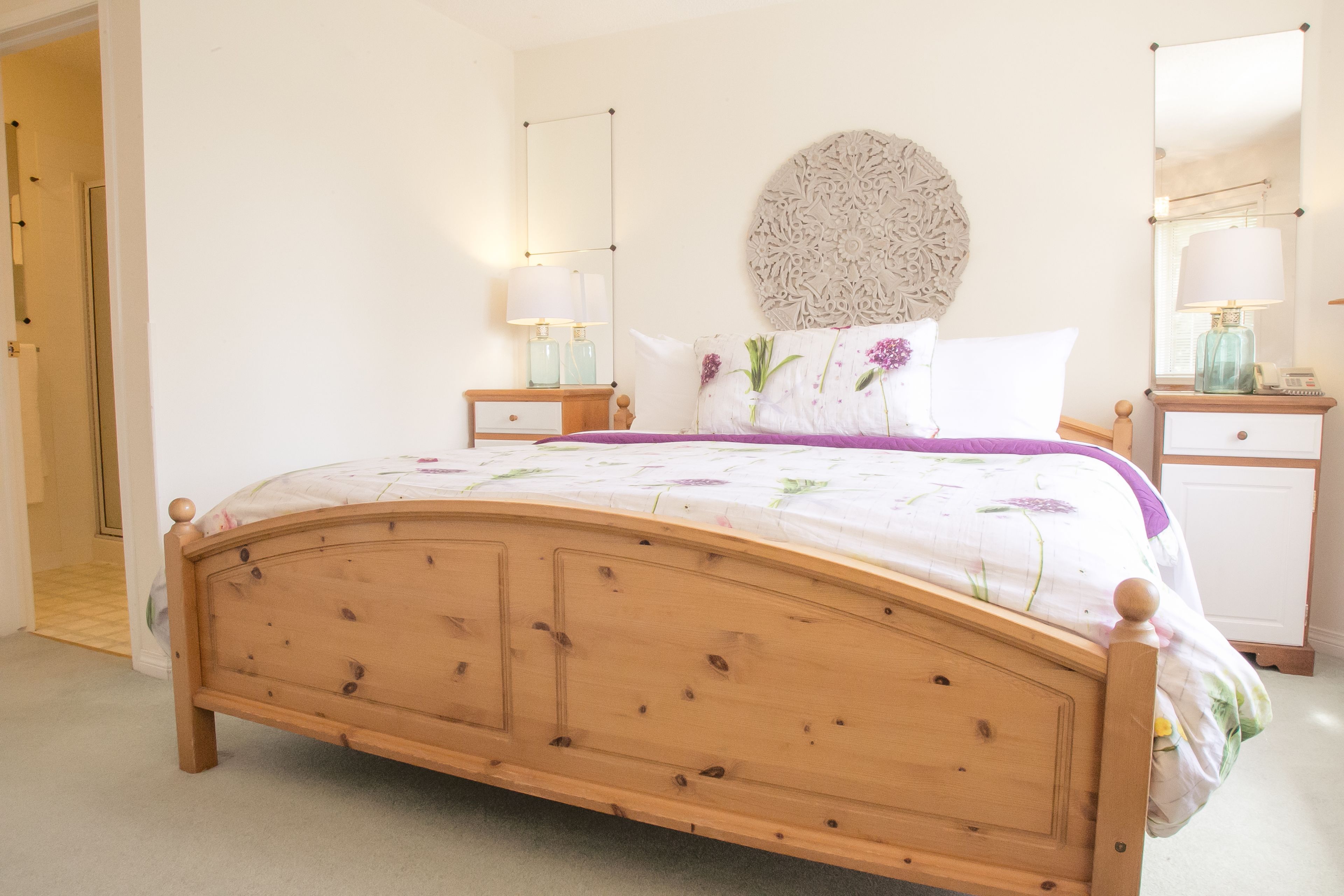 A bedroom with a wooden bed, a round decorative wall piece, two bedside tables with lamps, and a nightstand.