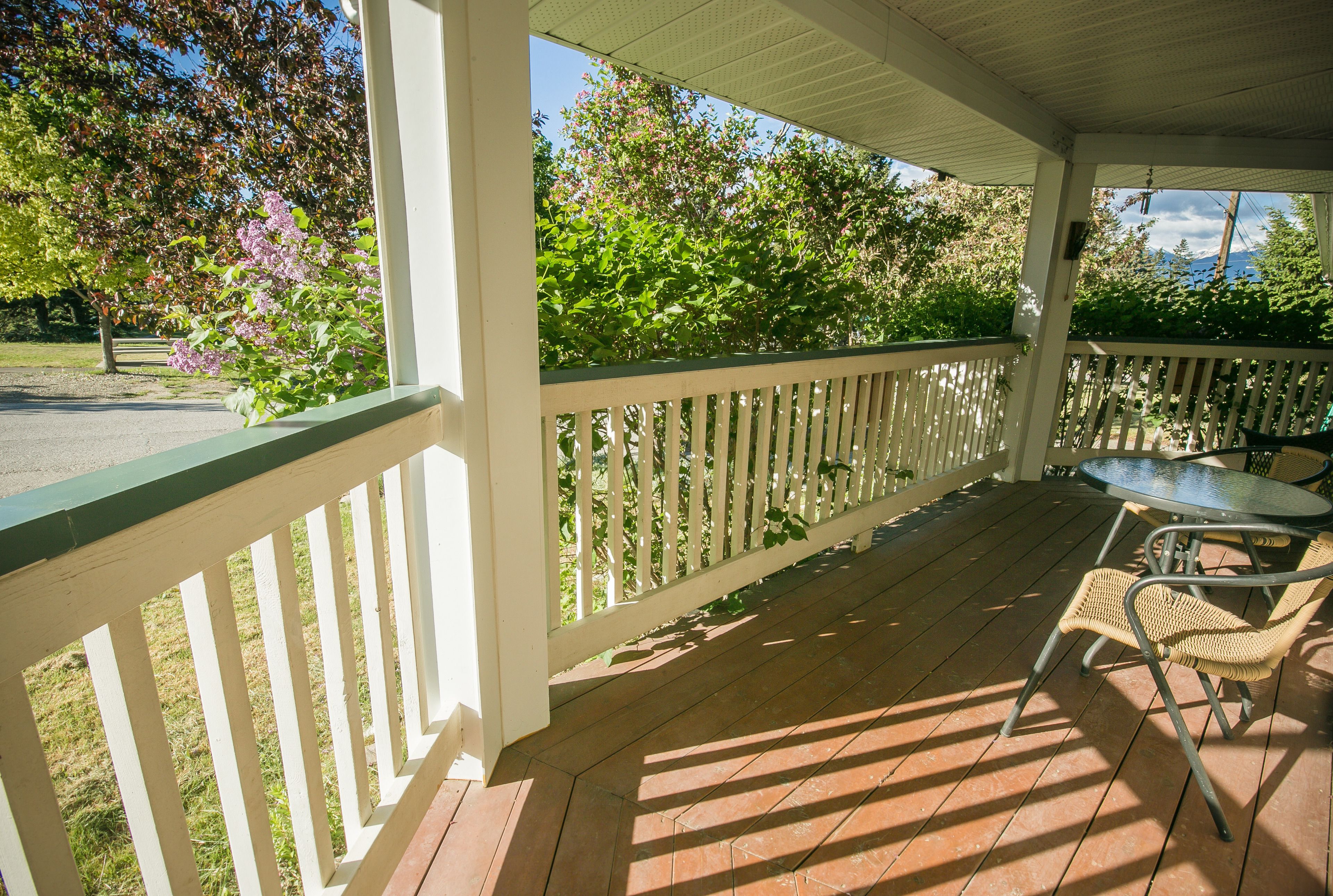A covered porch with a white railing, a table, and chairs.