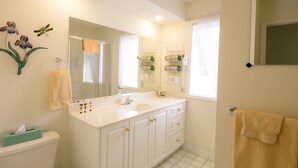 Un bagno con lavandino bianco, specchio e servizi igienici. Si notano fiori decorativi e un porta asciugamani.