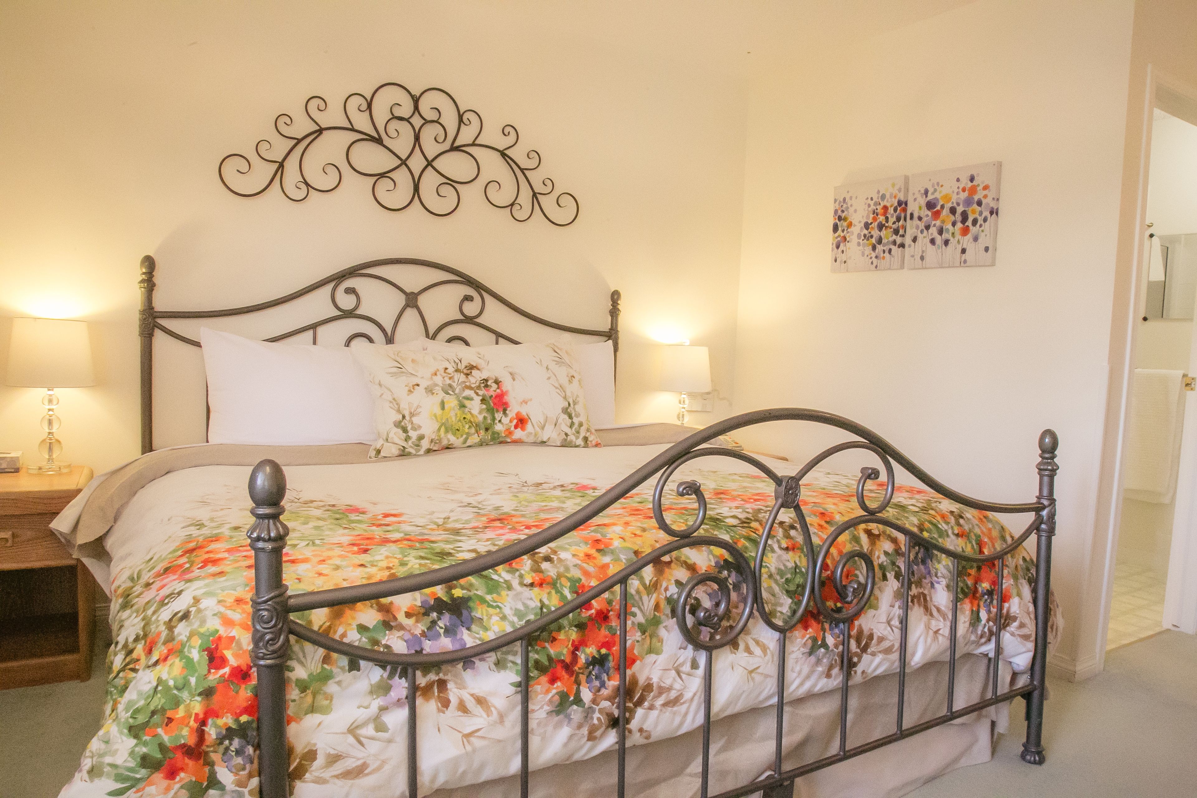 A neatly made bed with a floral bedspread, a decorative headboard, and two bedside lamps.