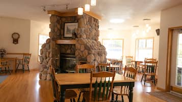 A dining area with a stone fireplace, wooden chairs, and a wooden table.