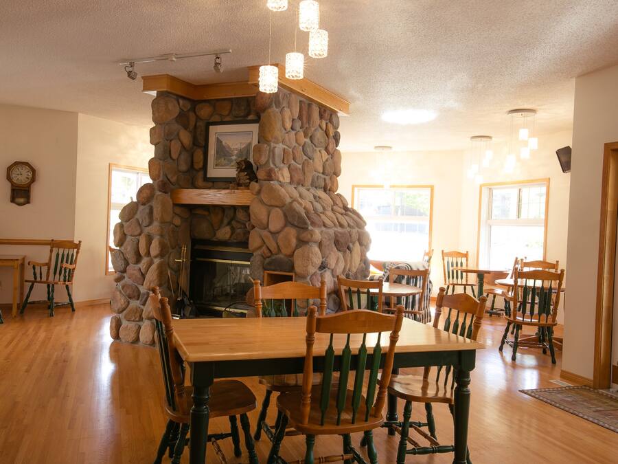 A dining area with a stone fireplace, wooden chairs, and a wooden table.