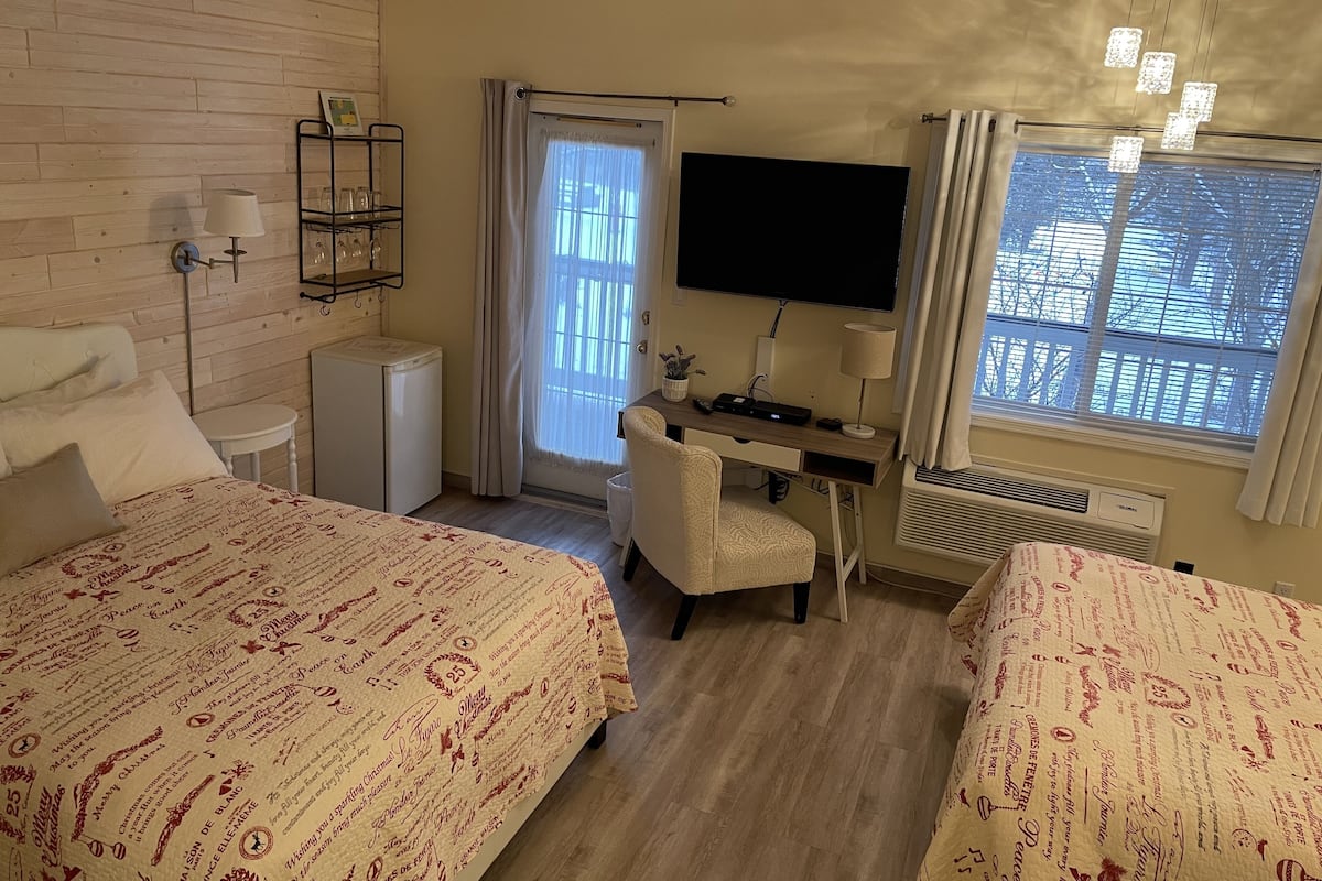 A hotel room with two beds, a desk, a TV, and a window with curtains.