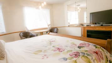 Habitación de hotel con cama, escritorio, silla, televisor y ventana con cortinas.