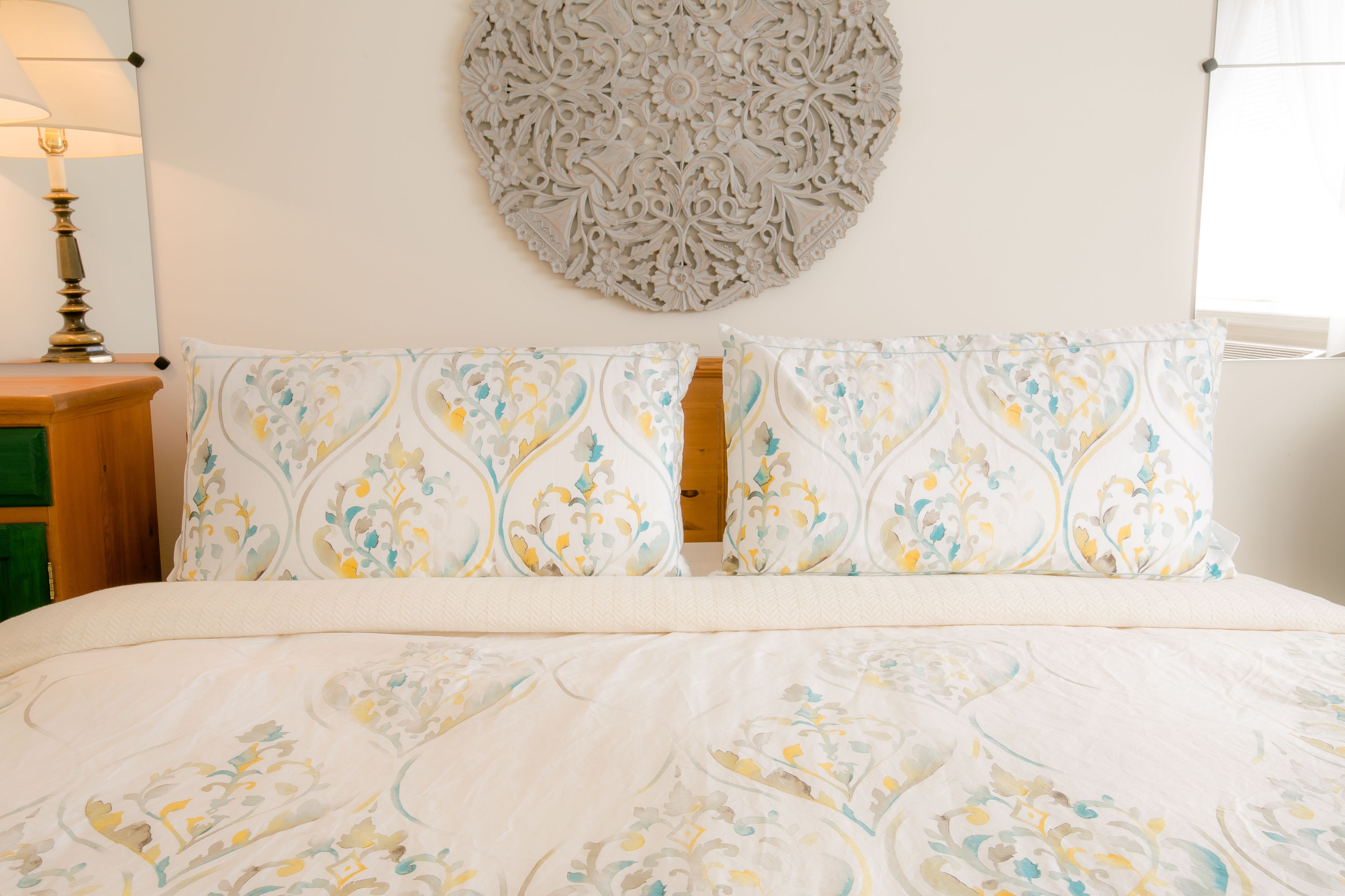 Una cama bien hecha con ropa de cama estampada, un tapiz decorativo y una lámpara de noche.
