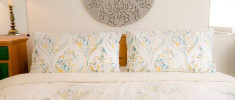Una cama bien hecha con ropa de cama estampada, un tapiz decorativo y una lámpara de noche.