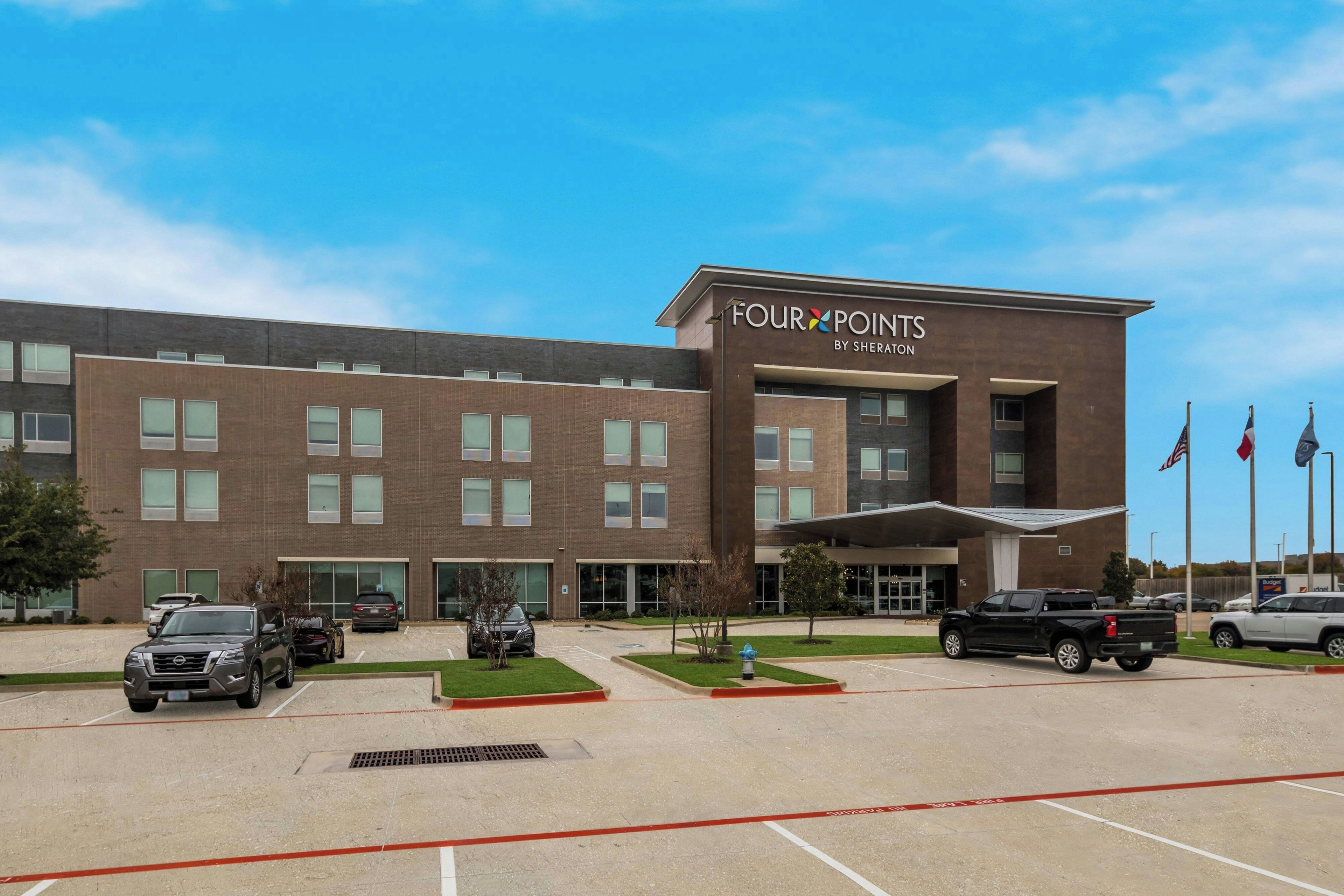 Ein Four Points by Sheraton Hotel mit Parkplatz und blauem Himmel.