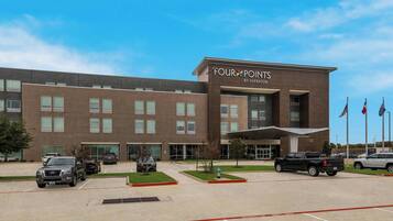 Ein Four Points by Sheraton Hotel mit Parkplatz und blauem Himmel.